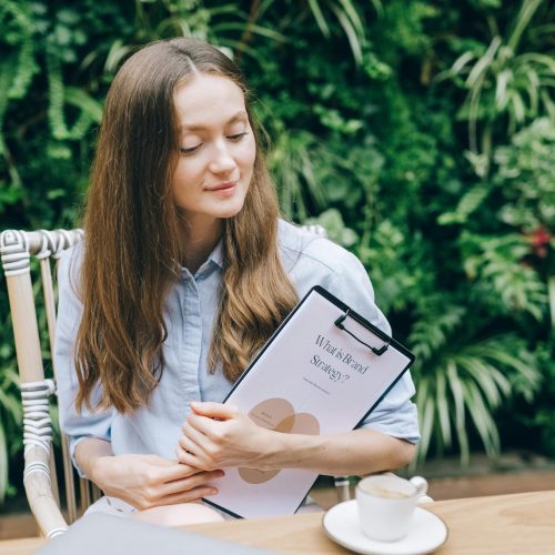 Young woman with clipboard enjoys coffee break in lush garden setting, symbolizing work-life balance.